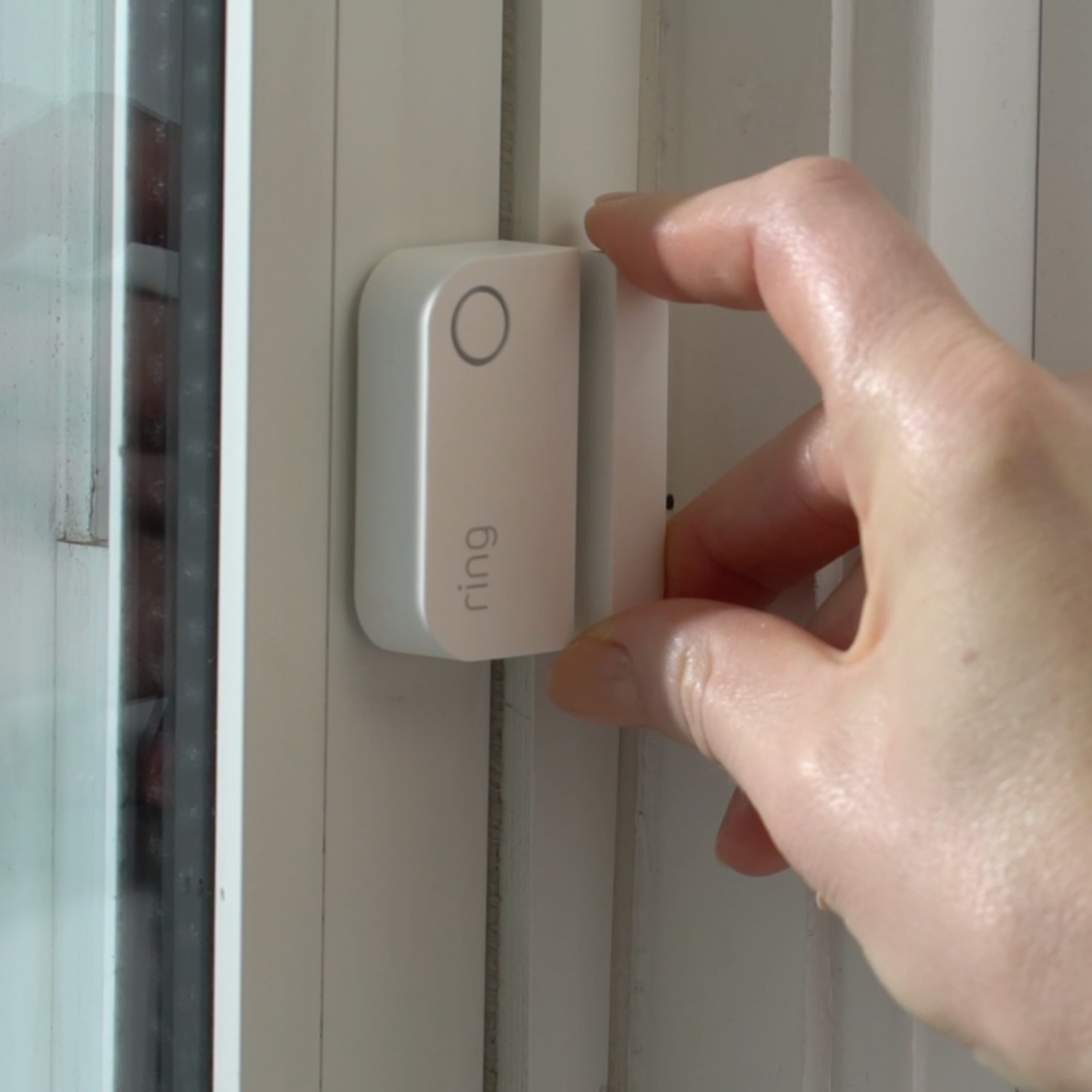 Alarm Window and Door Contact Sensor - Hand installing a white Ring Alarm Window and Door Contact Sensor on a window frame.