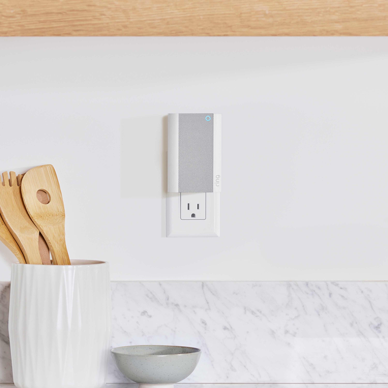 Chime Pro - Ring Chime Pro plugged into kitchen wall outlet near a grey bowl and a white ceramic utensil holder holding utensils.