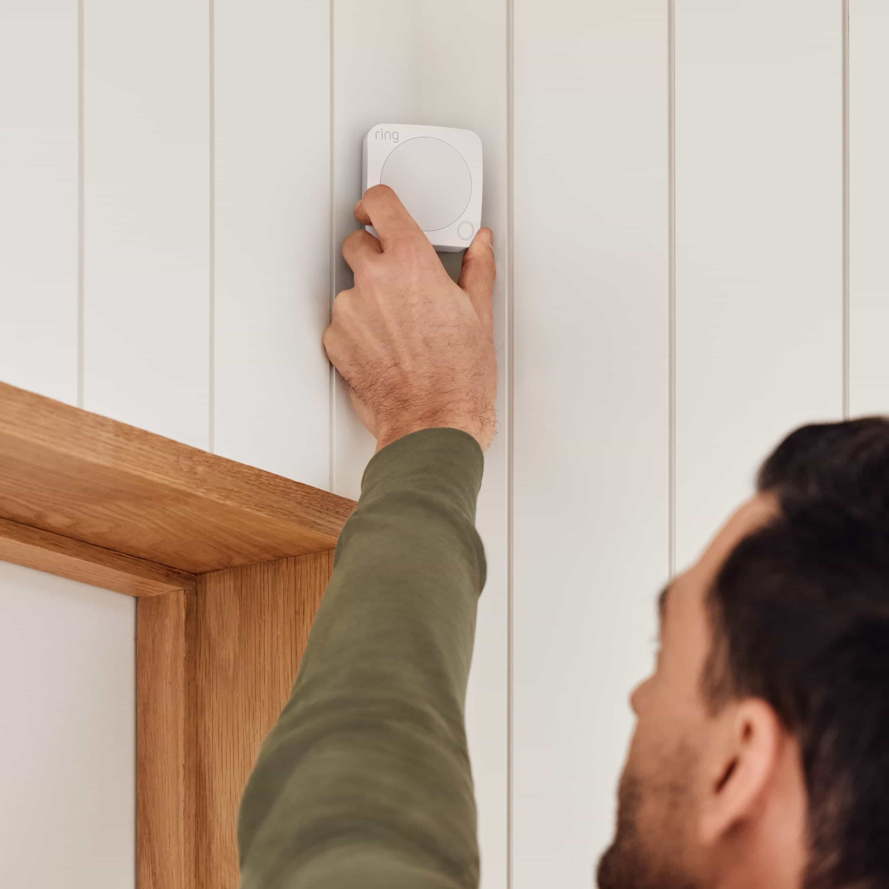 Alarm Security Kit, 5-Piece (for 2nd Generation) - Man installing a Ring Alarm Motion Detector on a wall above a doorway, showing easy setup of Ring Alarm Security Kit components for home protection.