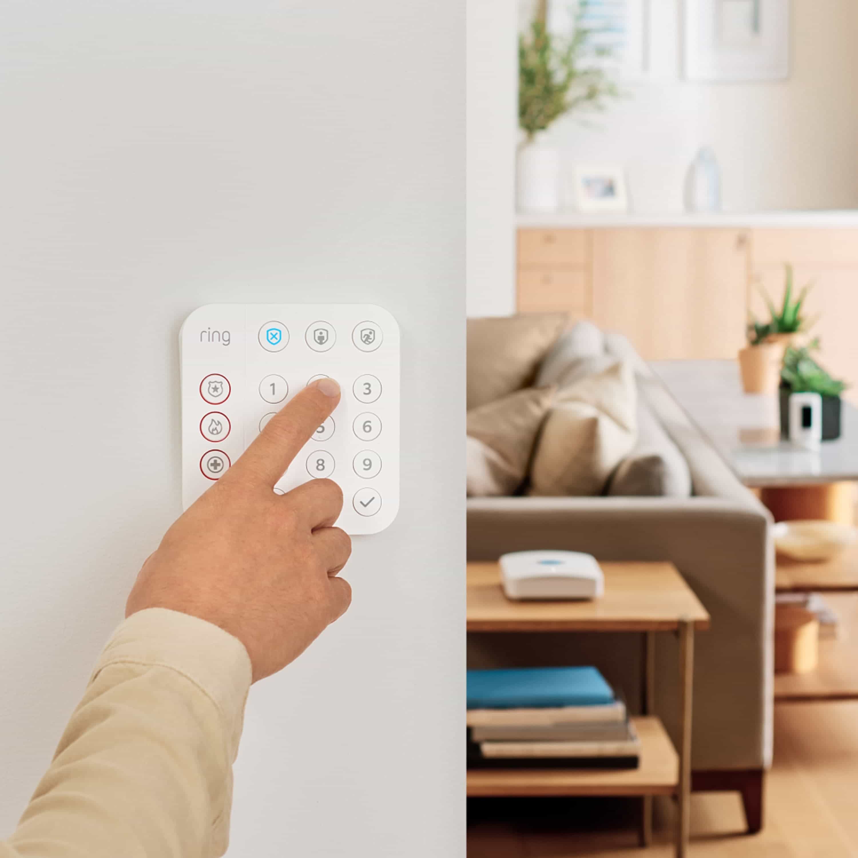 Alarm Security Kit, 5-Piece (for 2nd Generation) - Person pressing button on wall-mounted white Ring Alarm Keypad, with living room and Ring Base Station in background.