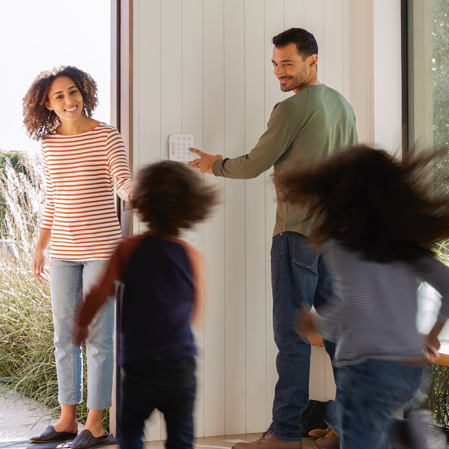 Alarm Security Kit, 14-Piece (2nd Generation) - Family exiting home as man uses a Ring Alarm Keypad on the wall, with two kids running toward a woman in doorway.