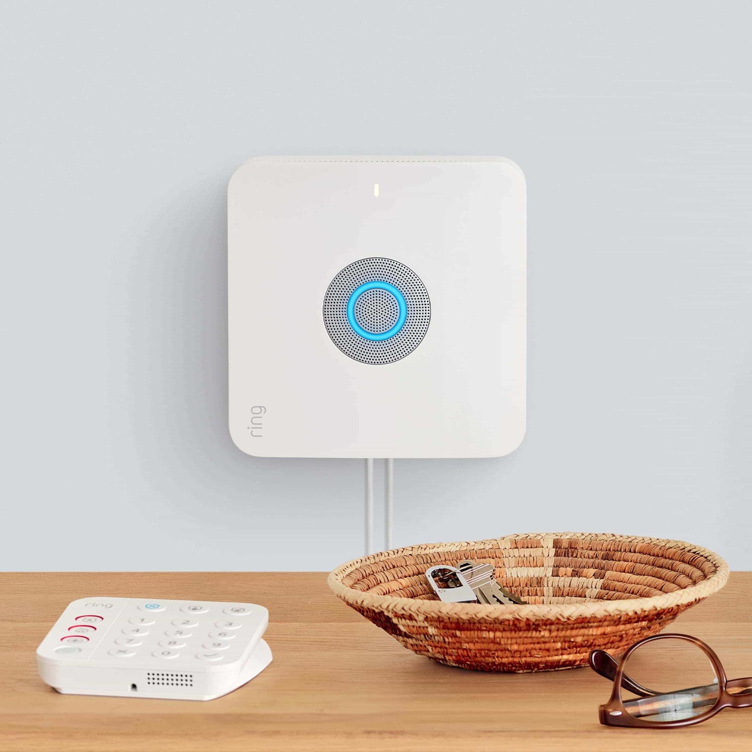 8-Piece Alarm Security Kit + Indoor Cam (2nd Gen) - wall-mounted Ring Alarm Base Station with glowing blue light, by Ring Alarm Keypad, a basket of keys, and glasses.
