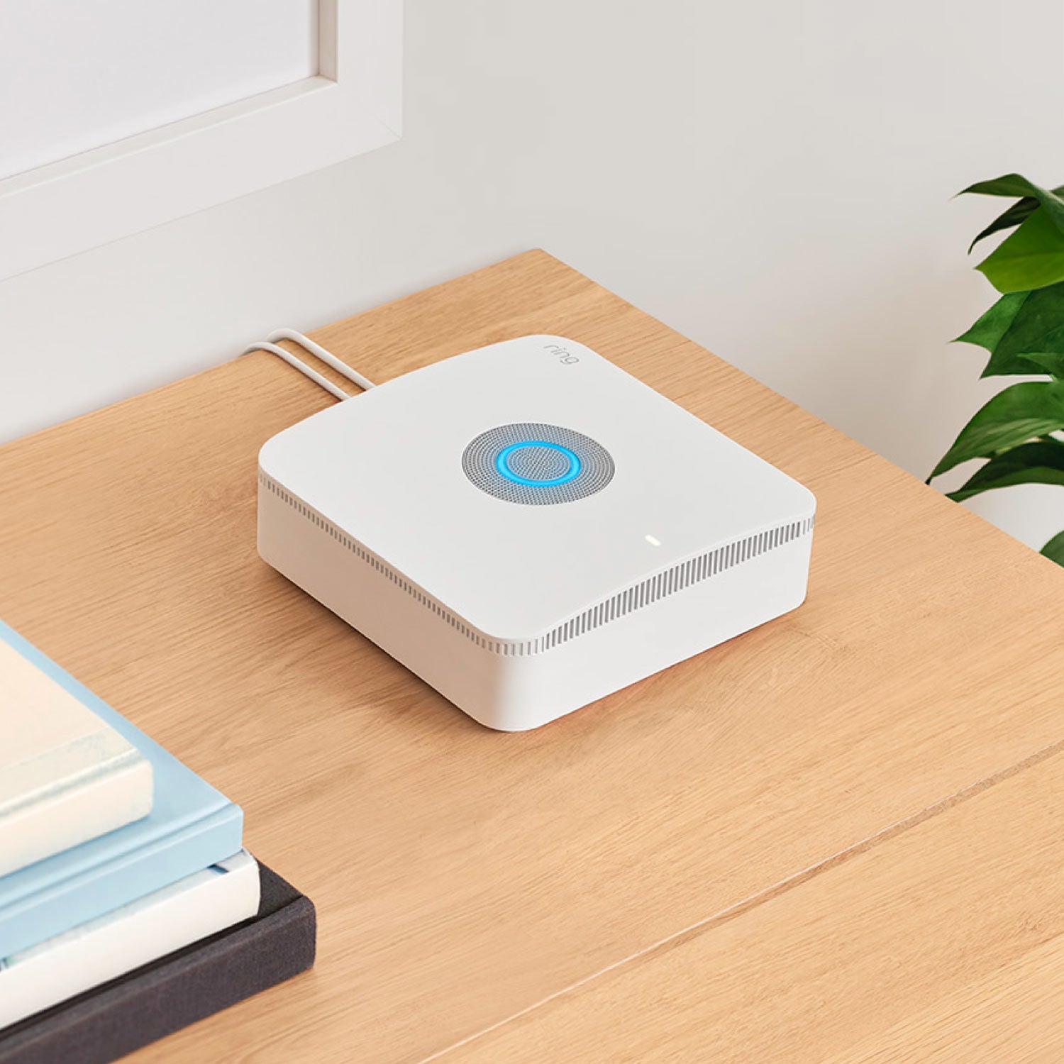 Alarm Pro, 13-Piece Kit (with built-in eero Wi-Fi 6 router and additional eero 6 Wi-Fi Router) - Ring Alarm Pro Base Station with glowing blue light and power cables extending from the back, on wooden table.