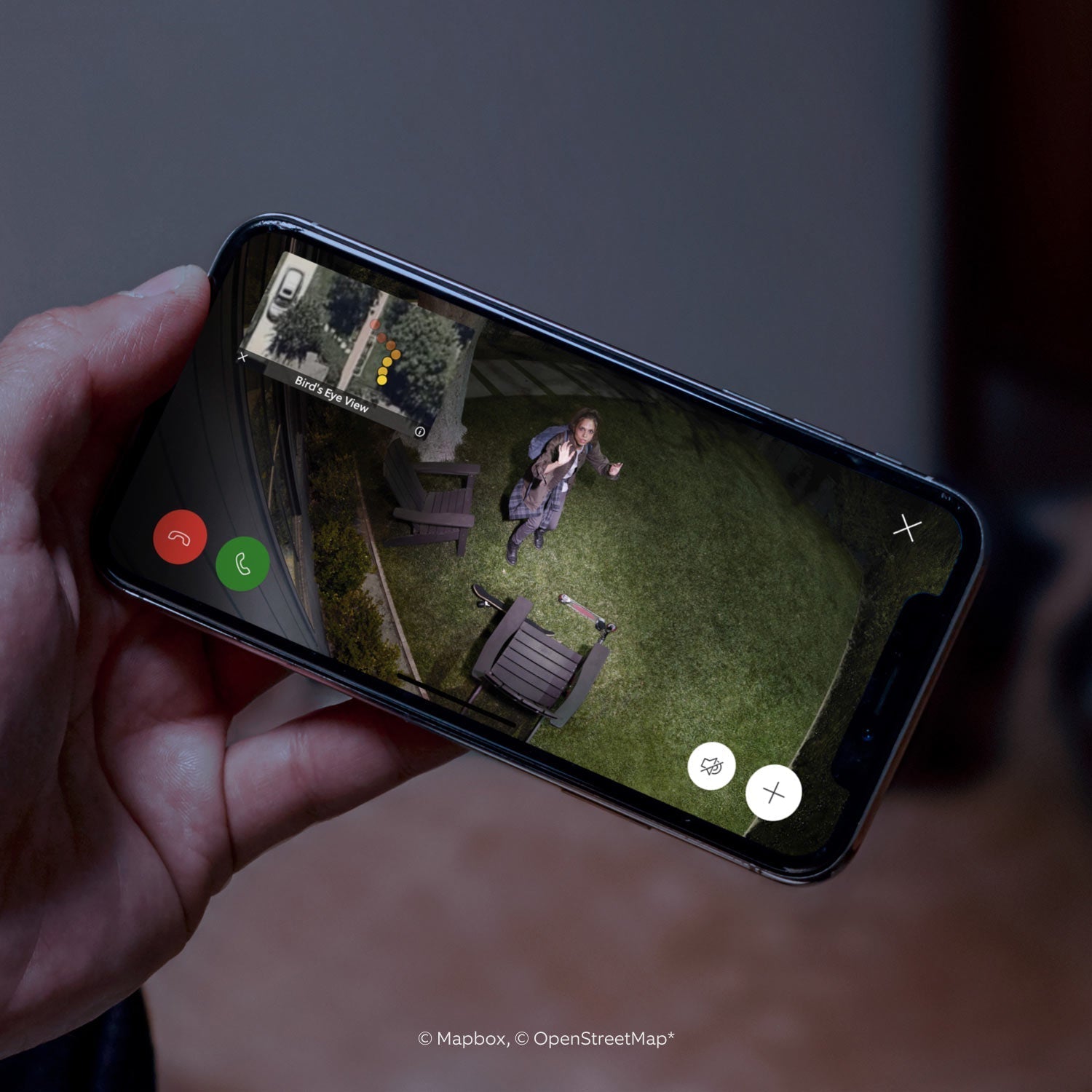 Spotlight Cam Pro (Featuring Retinal 2K) - Solar:Hand holding smartphone showing live Spotlight Cam Pro feed of a woman outside at night waving at the camera, with Bird's Eye View, call controls, and inset showing person's path. 