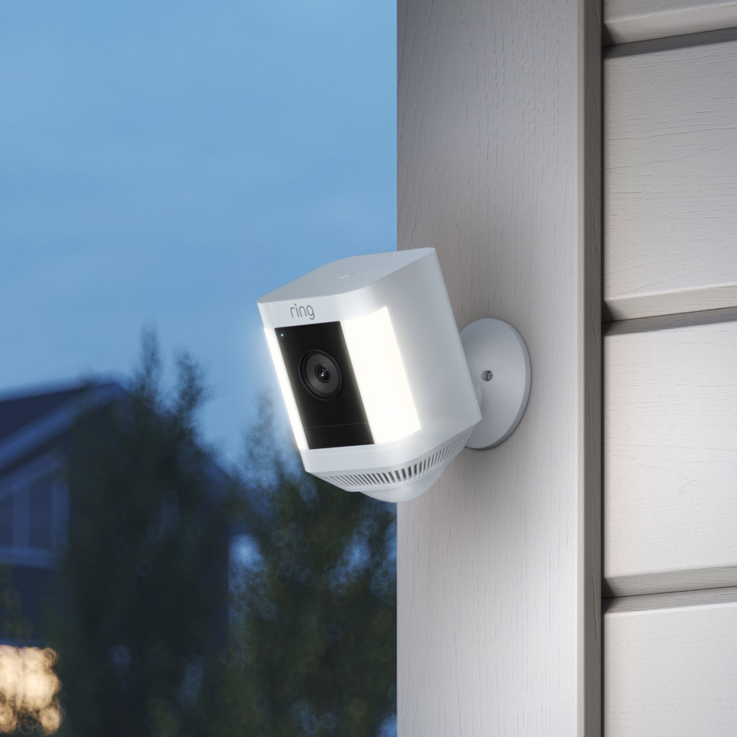 Bestselling Advanced Kit (Battery Doorbell Plus + Spotlight Cam Plus Battery) - Ring Spotlight Cam Plus mounted on an exterior wall, lit up at dusk with trees and houses in the background.