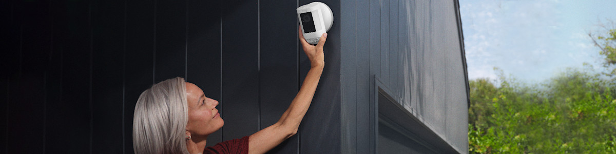 Person installing a white Ring security camera on a dark wall