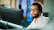 Professional wearing glasses smiles while working at computer monitors