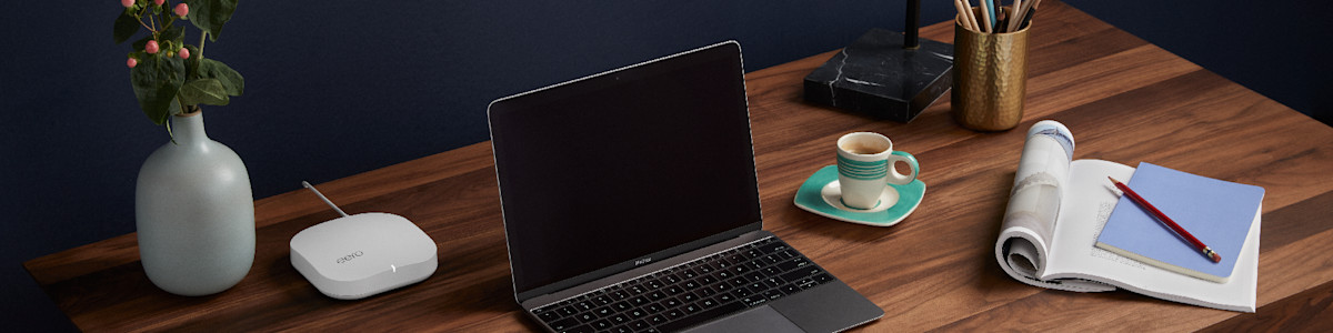 Laptop on wooden desk with coffee cup and grey vase with pink flowers